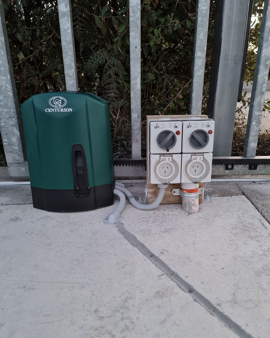 Gate motor and weatherproof control boxes installed at a residential driveway entrance in Millwater, Auckland