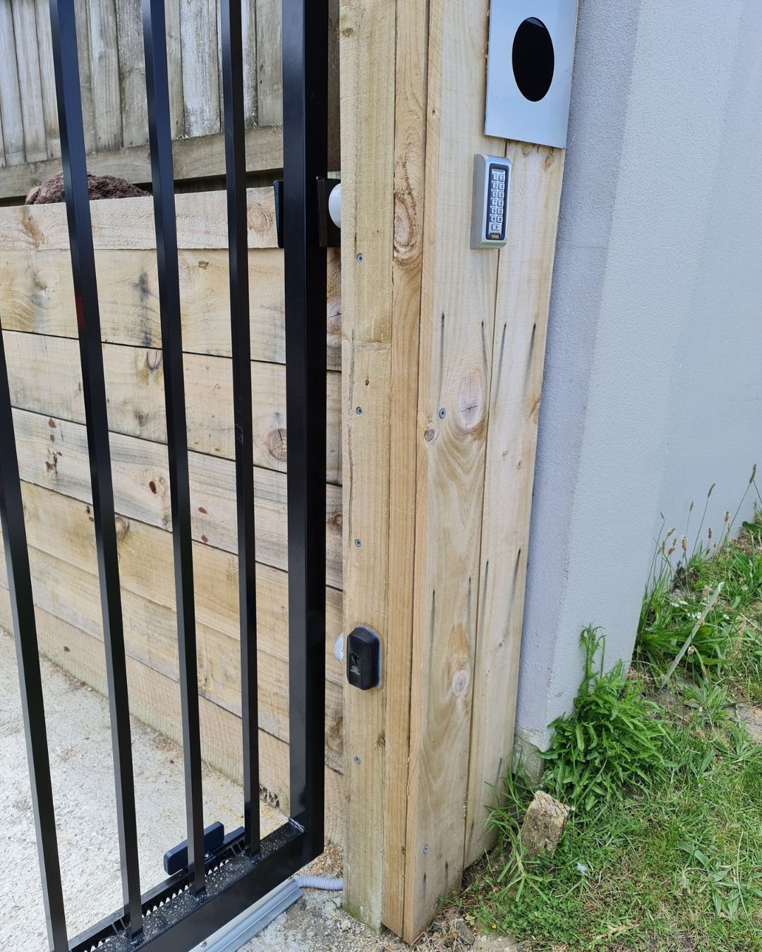 Gate entry keypad installed on a pillar beside a black wrought iron driveway gate, North Shore Auckland